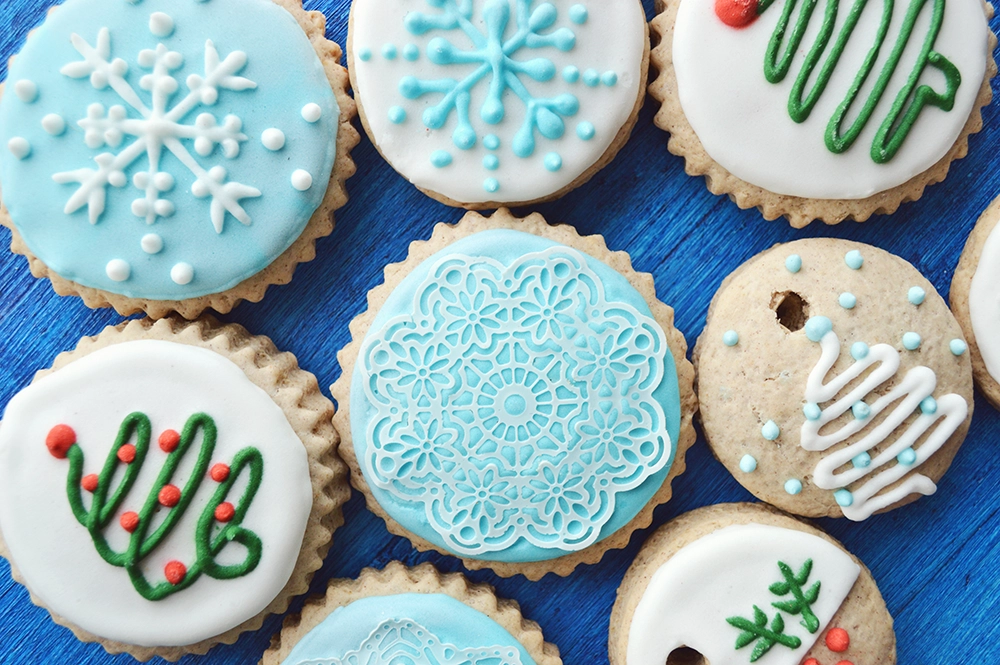 Festive holiday sugar cookie cutouts with icing and sprinkles on a decorative plate.