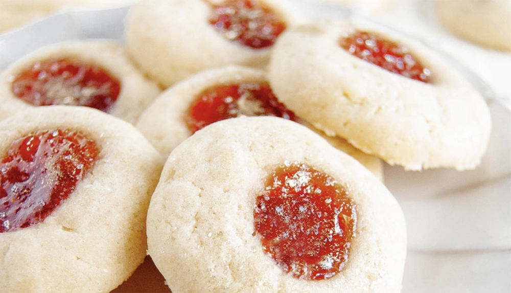 Holiday Thumbprint Cookies with jam and powdered sugar on a festive plate.