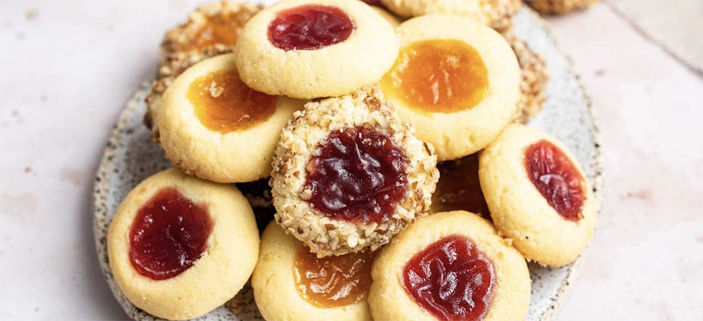 Holiday Thumbprint Cookies with jam and powdered sugar on a festive plate.